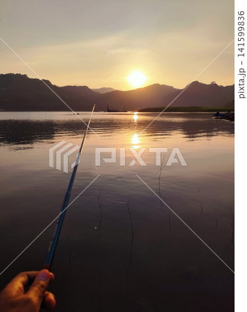 a person is fishing in a mountain lake at sunset a person is fishing in a mountain lake at sunset 141599836