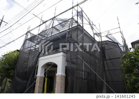 黒い養生ネットと足場に組まれた外壁塗装・リフォーム中の戸建て住宅 141601245