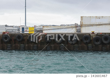 An industrial harbor dock lined with large tire fenders and stacked shipping containers An industrial harbor dock lined with large tire fenders and stacked shipping containers 141601467