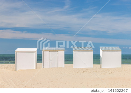 Minimalist Row of White Beach Huts on a Golden Sandy Shore Under a Vibrant Blue Sky with Turquoise Sea Horizon. Nieuwpoort town in Belgium, Europe. Minimalist Row of White Beach Huts on a Golden Sandy Shore Under a Vibrant Blue Sky with Turquoise Sea Horizon. Nieuwpoort town in Belgium, Europe. 141602267