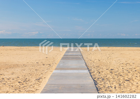 Wooden boardwalk path leading to the vast blue sea with golden sand under a clear sky on a sunny day at the beach. Ostend, a coastal city in Belgium, Europe. Wooden boardwalk path leading to the vast blue sea with golden sand under a clear sky on a sunny day at the beach. Ostend, a coastal city in Belgium, Europe. 141602282