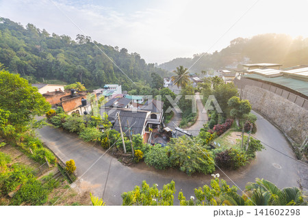 Panoramic high-angle view of a serene hillside village nestled in lush green mountains under soft morning sunlight, showcasing a peaceful tropical landscape. Kandy town in Sri Lanka. 141602298