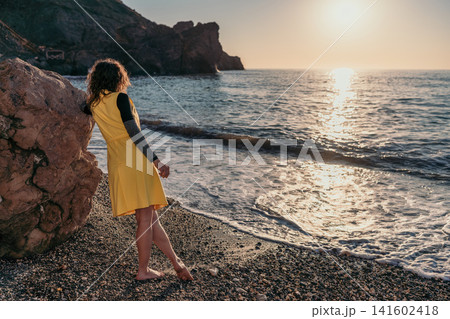Woman beach sunset overlooking the ocean while leaning on a rock at dusk Woman beach sunset overlooking the ocean while leaning on a rock at dusk 141602418