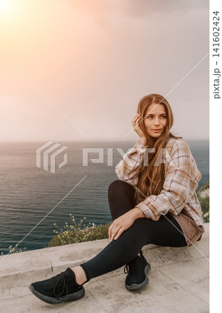Woman sunset ocean sitting on a stone wall overlooking the sea with copy space for inspirational text Woman sunset ocean sitting on a stone wall overlooking the sea with copy space for inspirational text 141602424