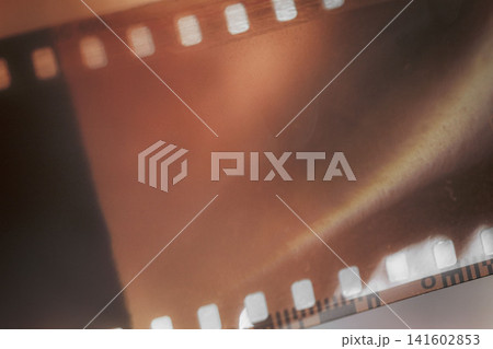 Vintage Photographic Film Negative, Copy Space. Close-up of translucent orange photographic film negative, perforated edges, soft shadows. Analog grainy photography background, warm sepia tones Vintage Photographic Film Negative, Copy Space. Close-up of translucent orange photographic film negative, perforated edges, soft shadows. Analog grainy photography background, warm sepia tones 141602853