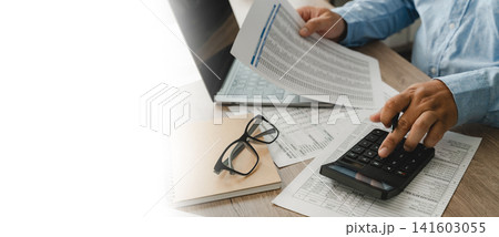 Hands hold a financial document and press a calculator beside a laptop, showing bookkeeping and budgeting workflow on paperwork with copy space for accounting, bookkeeping, and finance content. 141603055