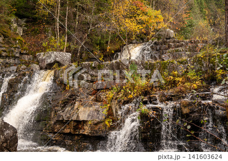 Scenic autumn waterfall in forest with cascading rocks and colorful foliage Scenic autumn waterfall in forest with cascading rocks and colorful foliage 141603624