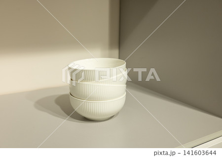 Stacked white ceramic bowls on neutral shelf in minimalist kitchen 141603644