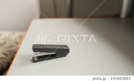Black stapler on a gray table with wooden edge in a minimalist office setting Black stapler on a gray table with wooden edge in a minimalist office setting 141603663