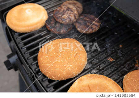 Grilled burgers and toasted buns on outdoor barbecue grill Grilled burgers and toasted buns on outdoor barbecue grill 141603684
