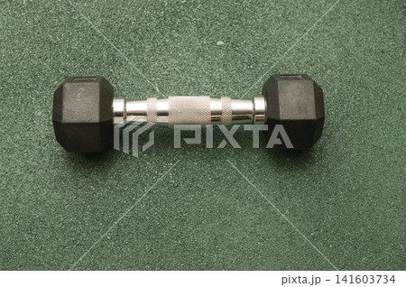 Black hex dumbbell on green gym floor for strength training and fitness workouts 141603734