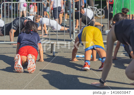 Warm-up. Young participants perform floor exercises behind barriers during the warm-up for the Become a Hero obstacle race Warm-up. Young participants perform floor exercises behind barriers during the warm-up for the Become a Hero obstacle race 141603847