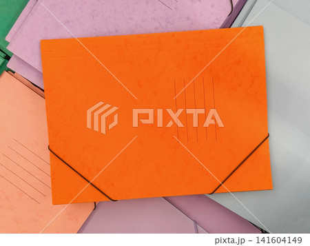 Bright orange cardboard document folder with elastic closure surrounded by pastel office folders. Colorful stationery composition for filing, organization, education and back to school designs Bright orange cardboard document folder with elastic closure surrounded by pastel office folders. Colorful stationery composition for filing, organization, education and back to school designs 141604149