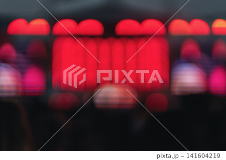 Abstract red stage lights glow above dark blurred audience silhouettes at live entertainment venue. Defocused illumination, bright dramatic background, copy space 141604219