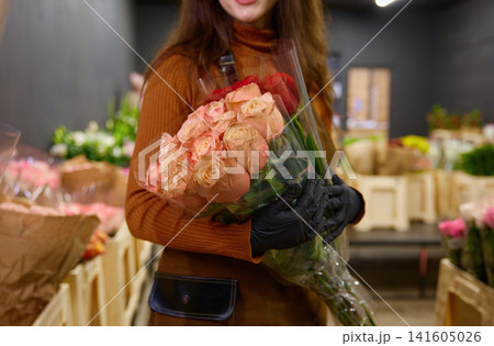 Caucasian florist carefully arranging peach and red flower stems in warm retail space 141605026