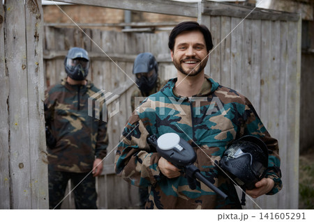Portrait of a smiled soldier holding his weapon and a helmet with other soldiers on the background Portrait of a smiled soldier holding his weapon and a helmet with other soldiers on the background 141605291