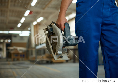 Skilled carpenter equipped with power tool amid workshop environment with blurred storage racks Skilled carpenter equipped with power tool amid workshop environment with blurred storage racks 141605713