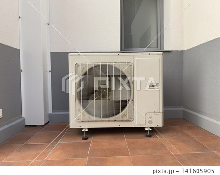 White outdoor air conditioning condenser unit on a tiled terrace, front view White outdoor air conditioning condenser unit on a tiled terrace, front view 141605905
