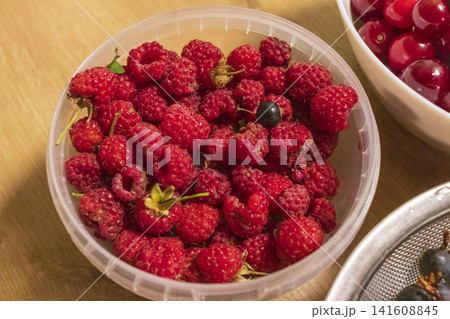 Ripe garden raspberries with a single stray blackcurrant in a round bucket 141608845