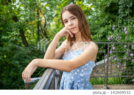 Portrait of a teenage girl in a blue floral dress leaning on a balcony railing in summer Portrait of a teenage girl in a blue floral dress leaning on a balcony railing in summer 141609532