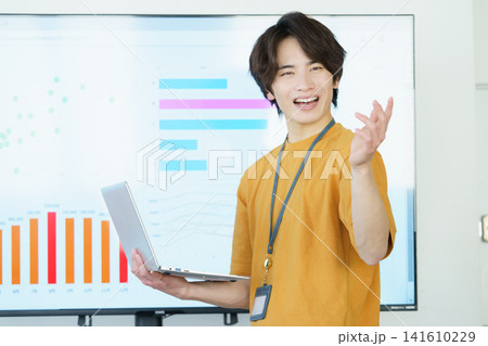 ノートパソコンを片手にプレゼンする若いカジュアルな服の日本人男性 ノートパソコンを片手にプレゼンする若いカジュアルな服の日本人男性 141610229