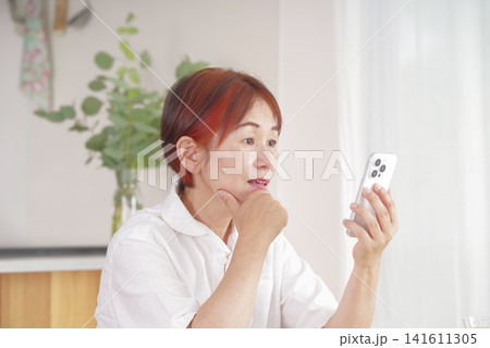 スマートフォンを見ながら悩む中高年女性 スマートフォンを見ながら悩む中高年女性 141611305
