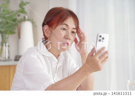 スマートフォンを見ながら悩む中高年女性 スマートフォンを見ながら悩む中高年女性 141611311