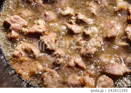 Chunks of meat are frying in hot oil in a kazan over a stove as part of the cooking process for plov in a home kitchen 141611393