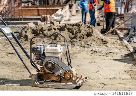 Construction workers use compactor during building project at construction site in daytime. Construction workers use compactor during building project at construction site in daytime. 141611617