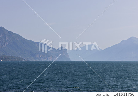 Telephoto Lake Garda view with hazy mountains and sailboats in sunny and hazy conditions 141611756