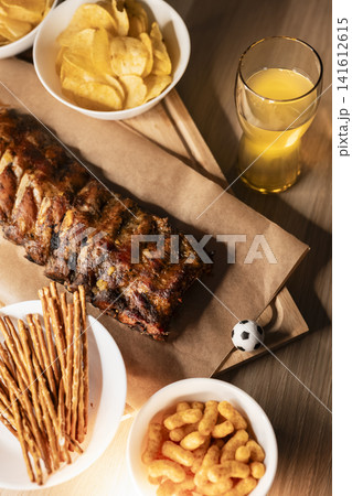 Barbecue ribs on a wooden board, beer and snacks arranged for a soccer viewing party, creating a cozy sport night atmosphere. Barbecue ribs on a wooden board, beer and snacks arranged for a soccer viewing party, creating a cozy sport night atmosphere. 141612615