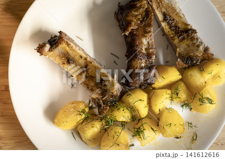 Roasted ribs with potatoes and dill served on a wooden table, conveying a rustic and hearty atmosphere of European kitchen. Roasted ribs with potatoes and dill served on a wooden table, conveying a rustic and hearty atmosphere of European kitchen. 141612616