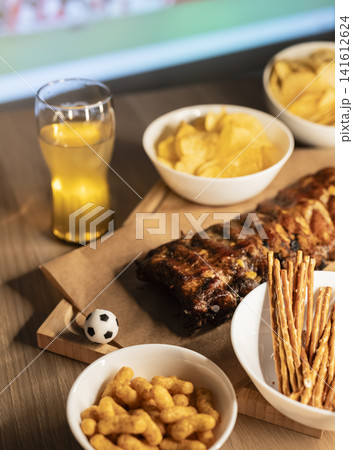 Grilled ribs on a wooden board with beer and snacks arranged for a soccer viewing party, illustrating food for big football events Grilled ribs on a wooden board with beer and snacks arranged for a soccer viewing party, illustrating food for big football events 141612624