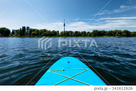 Turquoise paddleboard on water with modern city skyline, illustrating a relaxed summer water sport experience. Turquoise paddleboard on water with modern city skyline, illustrating a relaxed summer water sport experience. 141612626