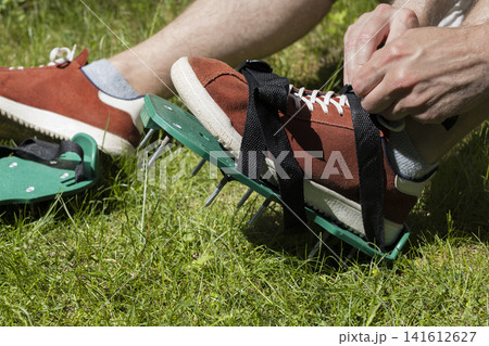 Person wearing lawn aerator shoes on grass, illustrating seasonal yard preparation and manual soil treatment for home garden care. Person wearing lawn aerator shoes on grass, illustrating seasonal yard preparation and manual soil treatment for home garden care. 141612627