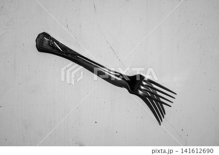Metal fork diagonally positioned over rough concrete surface in high contrast black and white 141612690