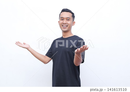 Young man smiles warmly with open arms. He wears a solid black t-shirt and stands against plain white background. His cheerful expression conveys openness and friendliness Young man smiles warmly with open arms. He wears a solid black t-shirt and stands against plain white background. His cheerful expression conveys openness and friendliness 141613510