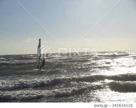 逆光の海でウィンドサーフィンを楽しむ人物と波が輝く海の風景 逆光の海でウィンドサーフィンを楽しむ人物と波が輝く海の風景 141614118