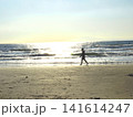逆光のビーチを歩くサーファーのシルエットと輝く海の風景 141614247