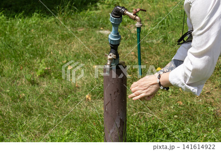 Rural garden hydrant for drawing water. A young woman is washing her hands. Rural garden hydrant for drawing water. A young woman is washing her hands. 141614922