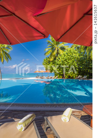 Stylish tropical poolside with red umbrella and sun loungers beside palm trees turquoise lagoon blue sky. Perfect summer vacation travel resort paradise. Luxury getaway relax scenic Stylish tropical poolside with red umbrella and sun loungers beside palm trees turquoise lagoon blue sky. Perfect summer vacation travel resort paradise. Luxury getaway relax scenic 141615637