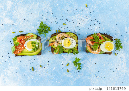 Healthy snack or appetizer toast with salmon, avocado, shrimps, eggs, cucumber, lambs lettuce or corn salad and parsley. Top view Healthy snack or appetizer toast with salmon, avocado, shrimps, eggs, cucumber, lambs lettuce or corn salad and parsley. Top view 141615769