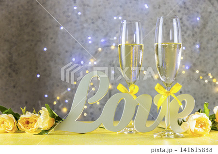 Two Champagne glasses with yellow bows standing on table with love letters and roses, bokeh lights, St. Valentine or wedding greeting card Two Champagne glasses with yellow bows standing on table with love letters and roses, bokeh lights, St. Valentine or wedding greeting card 141615838