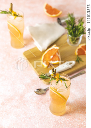 Two highball glasses of Paloma cocktails with tequila fresh grapefruit juice combined and rosemary. Surrounded of ingredients and bar tools. Light pink concrete surface. 141615878