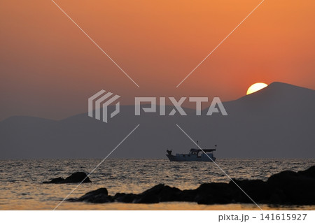 a lonely fishing boat in the sea as the sun sets behind the mountains a lonely fishing boat in the sea as the sun sets behind the mountains 141615927