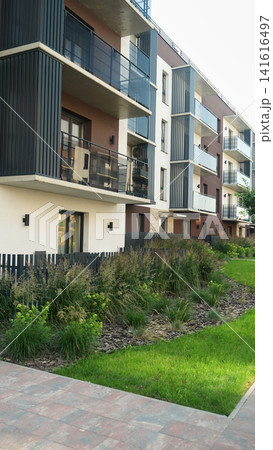 New apartment complex exterior showing multiple floors with stylish balconies, a lush garden, and walkway New apartment complex exterior showing multiple floors with stylish balconies, a lush garden, and walkway 141616497