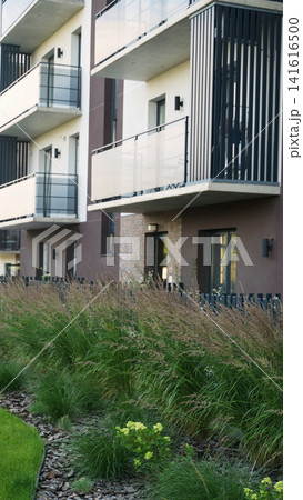 Modern residential building featuring balconies and a beautifully landscaped urban garden with tall grasses Modern residential building featuring balconies and a beautifully landscaped urban garden with tall grasses 141616500