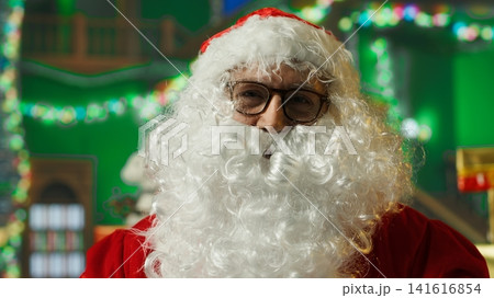 Portrait of entertainer dressed as Santa Claus wearing fake beard, red jacket and hat with white pompom. POV of man portraying Christmas character looking in mirror, adjusting glasses, camera A 141616854