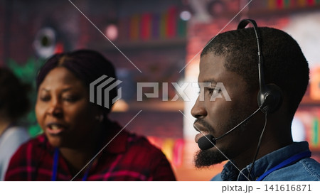 Call center coworkers in office helping customers regain access to accounts, resetting passwords. African american colleagues in customer center assisting clients needing help, camera A 141616871