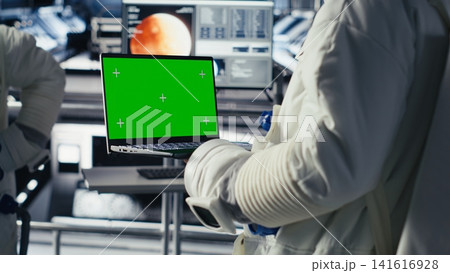 Astronaut monitoring system diagnostics on isolated screen laptop, chatting with colleague during space mission. Teamworking cosmonauts using mockup notebook during cosmic expedition Astronaut monitoring system diagnostics on isolated screen laptop, chatting with colleague during space mission. Teamworking cosmonauts using mockup notebook during cosmic expedition 141616928